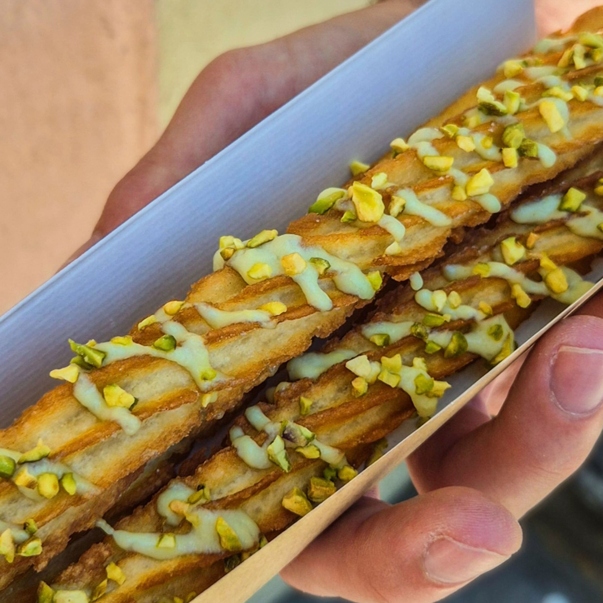 Longs churros artisanaux nappés d'une crème à la pistache et saupoudrés d'éclats de pistaches grillées