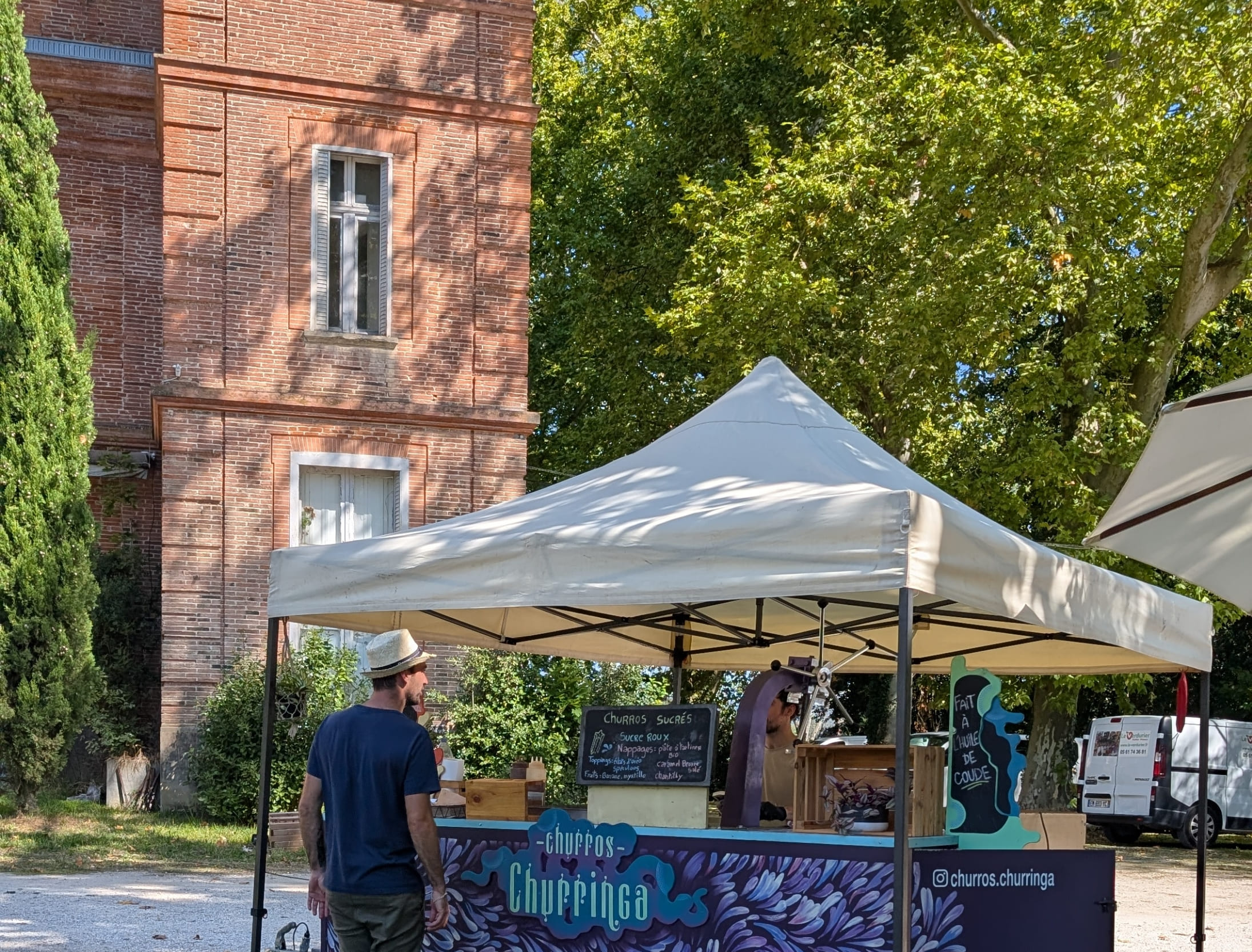 Stand de churros artisanaux 'Churringa' installé sous un barnum blanc lors d'un événement privé en extérieur devant une élégante bâtisse en briques rouges