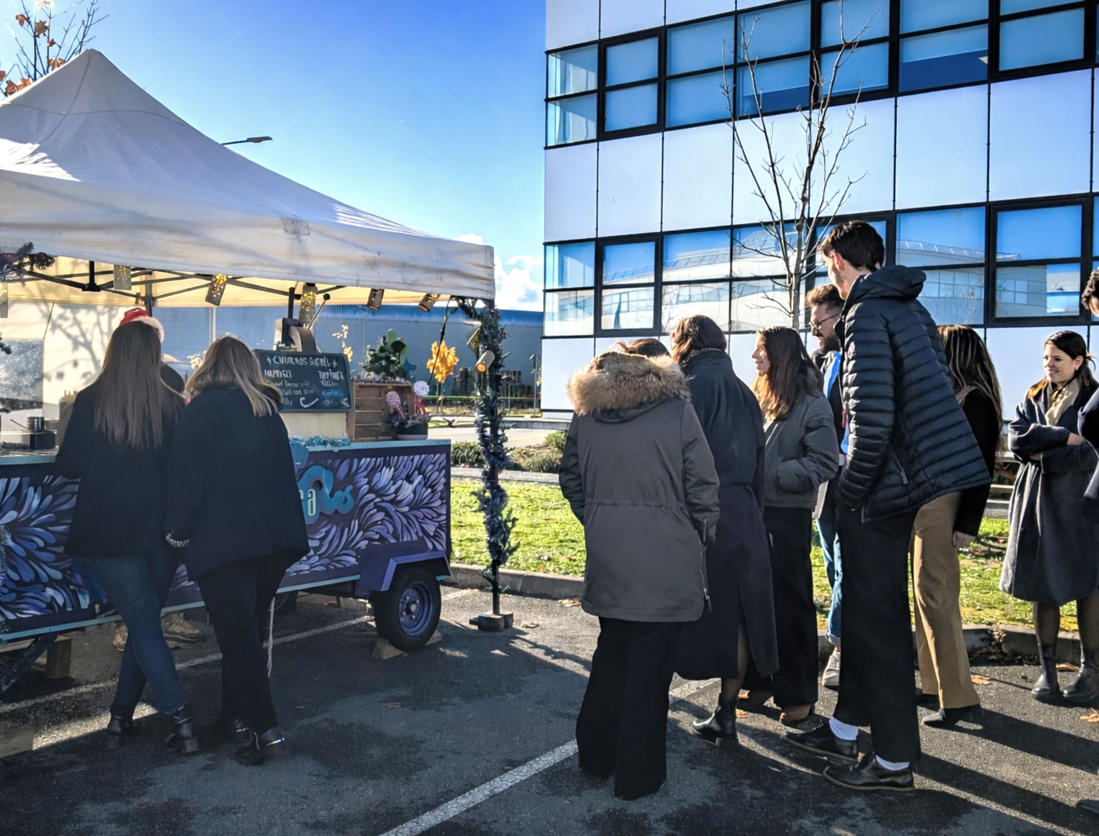 Prestation événementielle de l'entreprise Churringa : stand de churros installé sur le parking d'un bâtiment de bureaux moderne pour un goûter d'entreprise convivial.