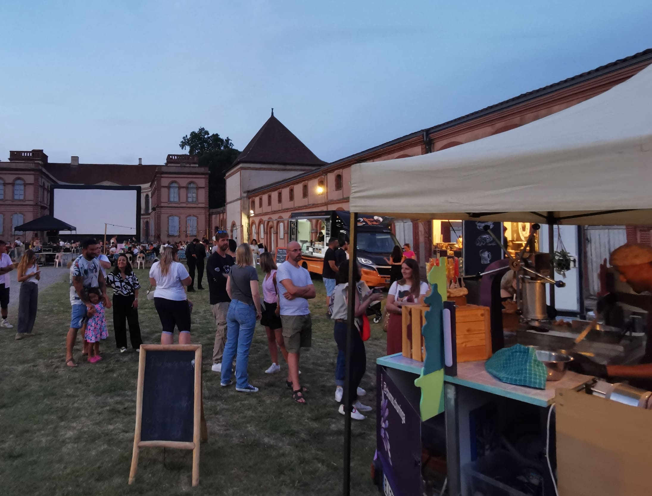 Stand de churros Churringa installé lors d'une séance de cinéma en plein air à la tombée de la nuit, avec une file d'attente de clients devant un château historique et un écran géant.