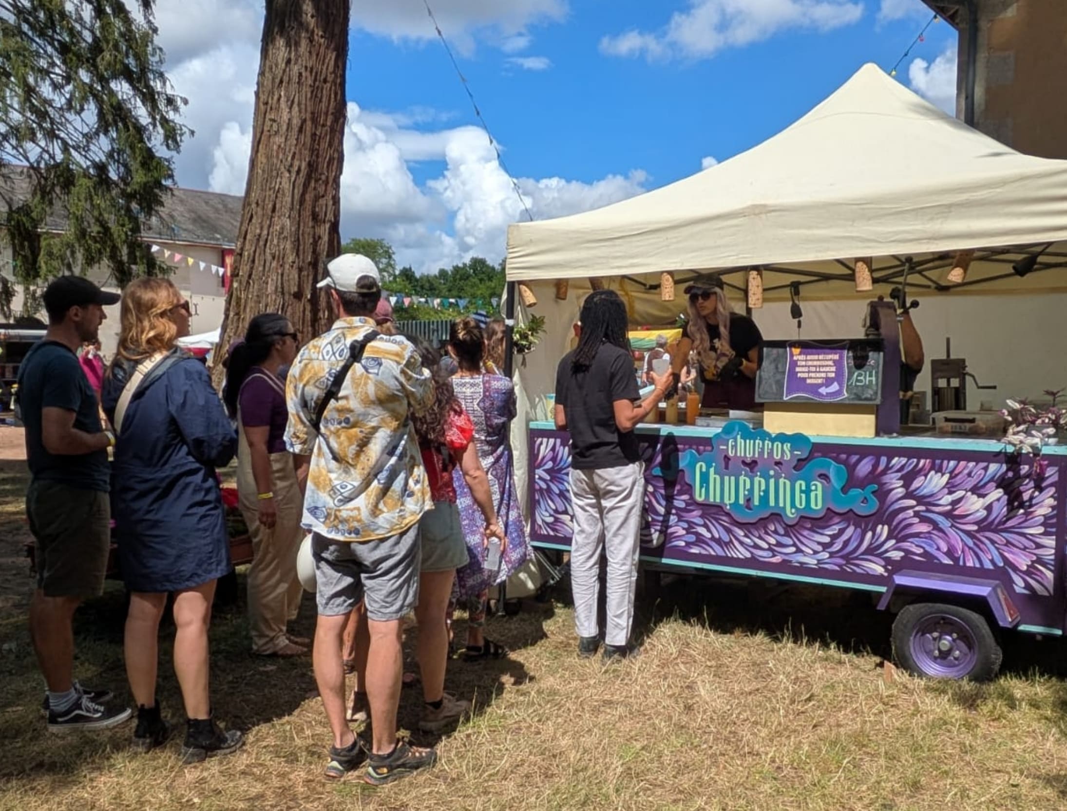 Moment de partage et de gourmandise au stand Churringa, proposant des churros vegan et bio dans un cadre naturel et joyeux décoré de fanions colorés.